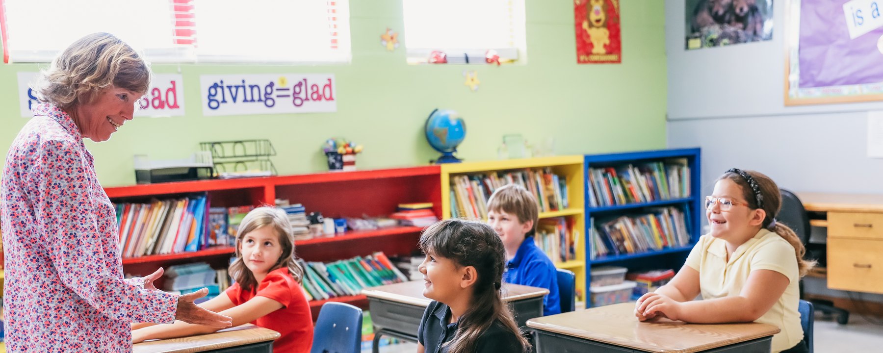 A teacher talking with four students at their desks in a Trinity Christian Academy classroom